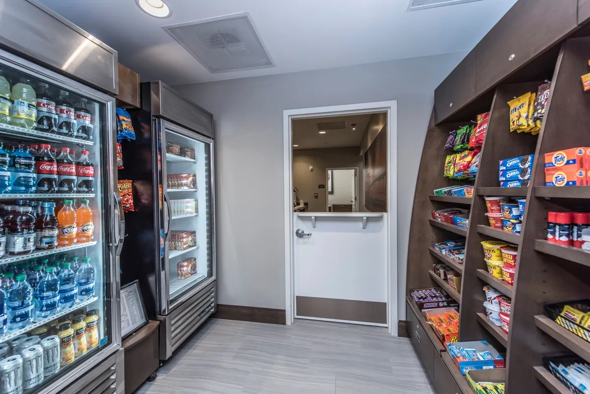 A cozy interior corner with a well-stocked refrigerated beverage display and snack shelves near the entrance, offering guests quick, convenient access to refreshments. The scene conveys a casual, welcoming mood, inviting guests to refuel after a day out.