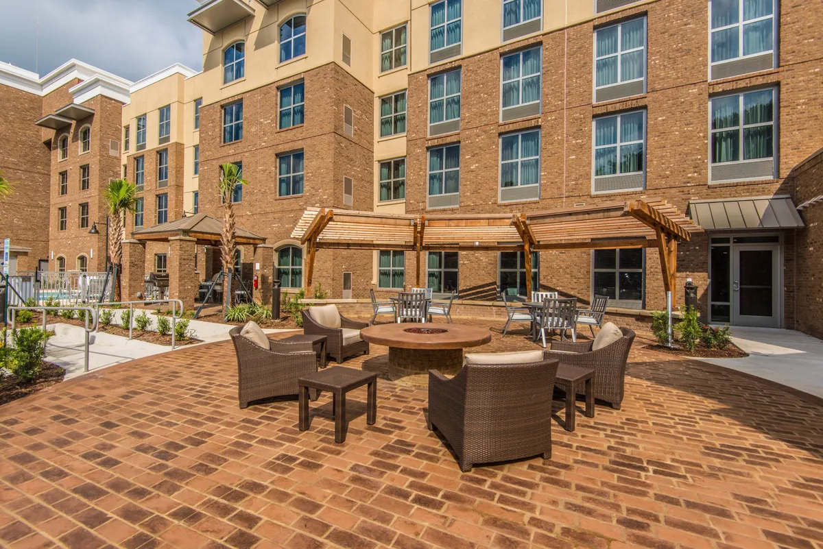 The image features a beautifully landscaped garden with a modern building facade in the background. A welcoming outdoor fire pit is surrounded by plush seating, inviting guests to relax and connect. The ambient lighting at sunset creates a romantic and relaxed atmosphere, perfect for evening gatherings or quiet moments after a day of exploration.