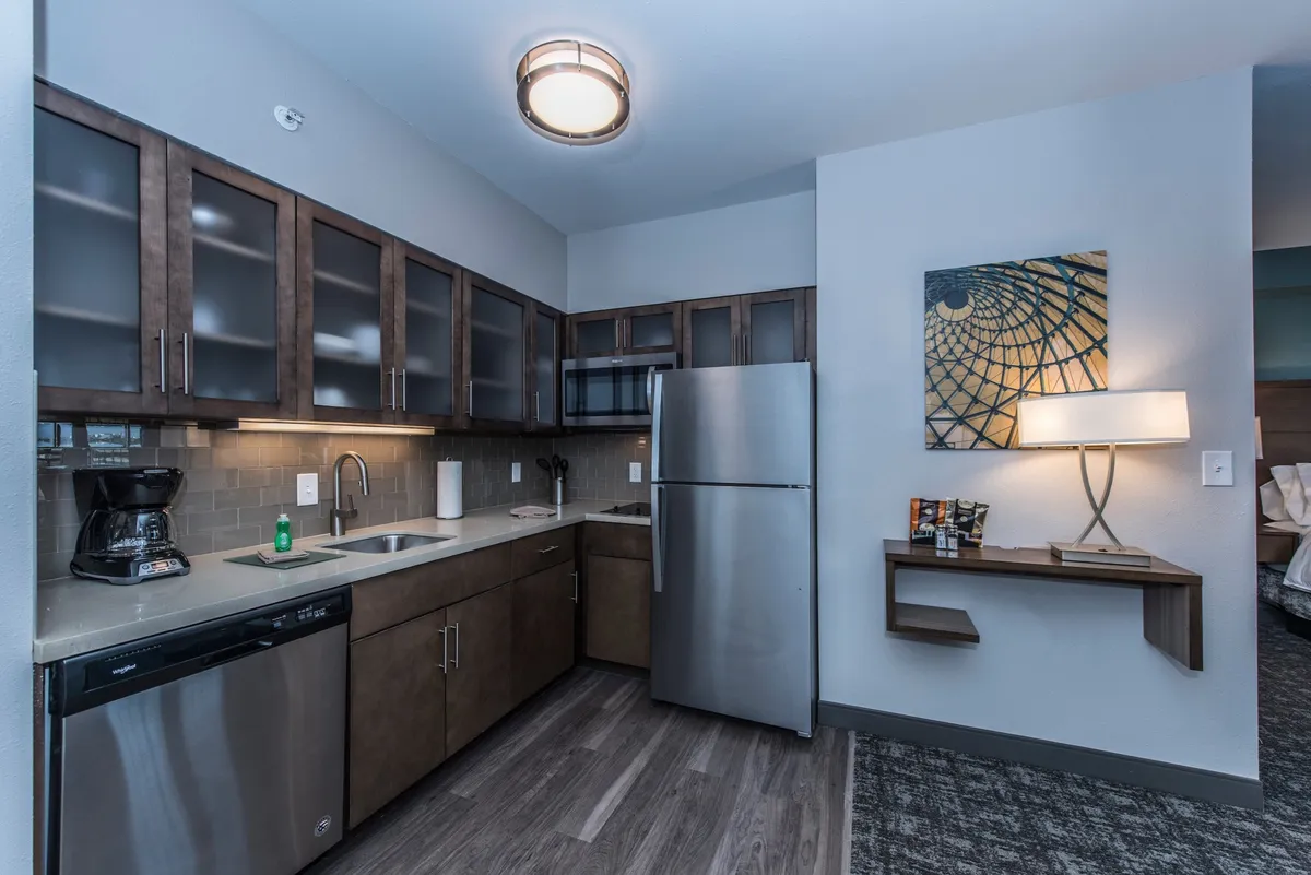 A modern kitchen with stainless steel fridge, dark cabinetry, kitchen sink, and a visible coffee maker, complemented by decorative wall art. The space appears functional and inviting, perfect for meal preparation and enjoying a fresh cup of coffee.