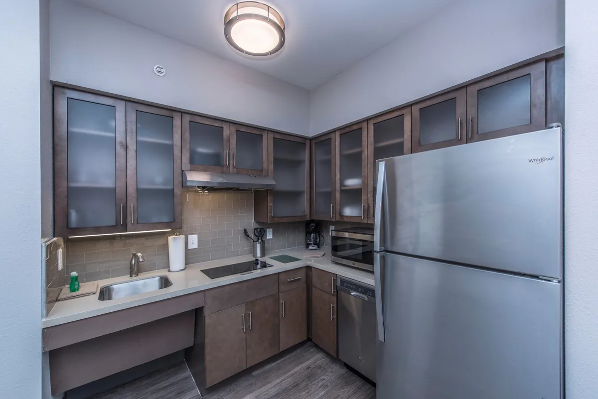 A contemporary kitchen space featuring a stainless steel refrigerator, modern cabinetry, a clean sink with faucet, and essential kitchen appliances. The layout is practical, emphasizing functionality for cooking and entertaining.
