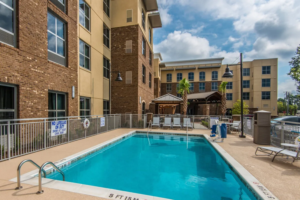 This exterior scene centers on a sparkling outdoor swimming pool bordered by lounge chairs and a poolside cabana, set against the backdrop of the hotel’s facade. The area is designed for both relaxing and social activities, with ample space for guests to swim, sunbathe, or participate in seasonal events.