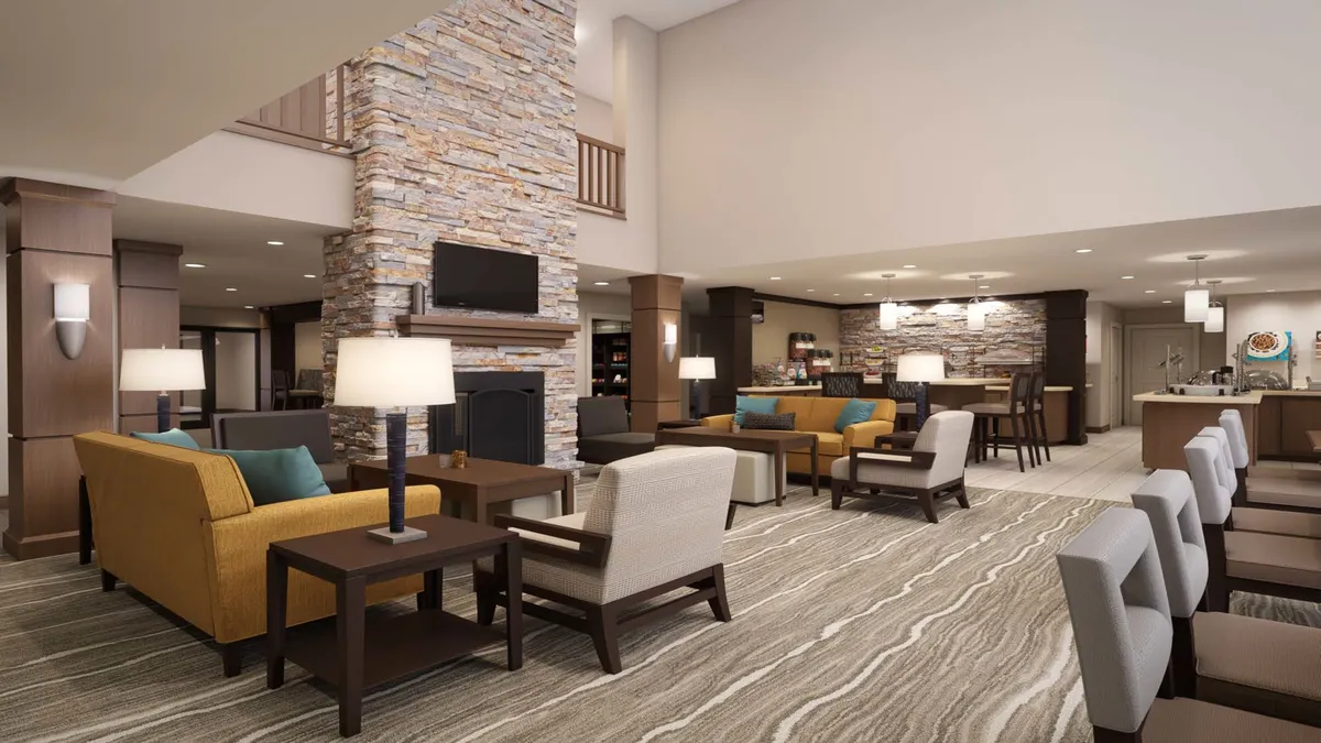 A stylish communal lounge with a stone fireplace, comfortable seating, and modern lighting. Guests are seen casually working on laptops or engaging in quiet conversation, highlighting the flexibility of the space for both productivity and relaxation.
